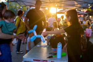 Woman giving balloon animal at sunset market.
